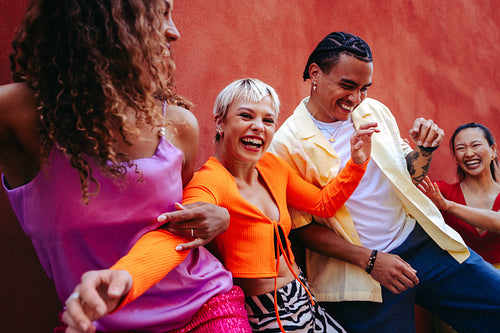 Young adult friends dance and laugh together outdoors by a colorful wall