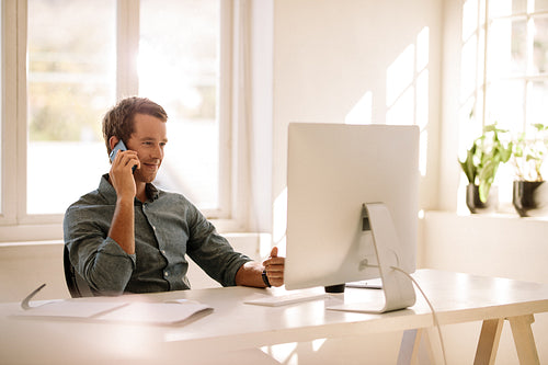 Entrepreneur talking on mobile phone while working on computer at home