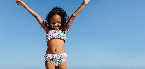 Happy child enjoying a summer beach vacation with arms raised against blue sky