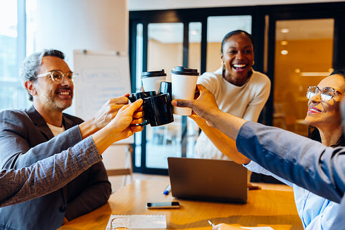 Group of colleagues toasting with coffee mugs during a cheerful office moment