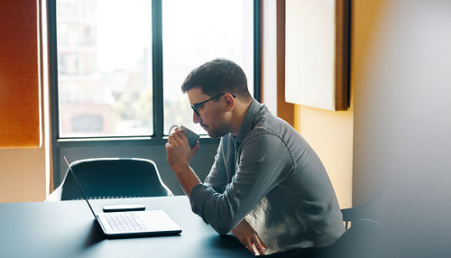 Man in a modern office working on a laptop and drinking coffee