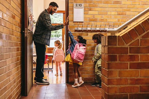 Elementary school teacher greeting his students at the door. Male teacher welcoming his class with a high five