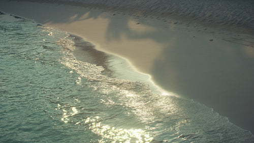 Gentle ocean waves washing a serene tropical beach with sparkling morning light
