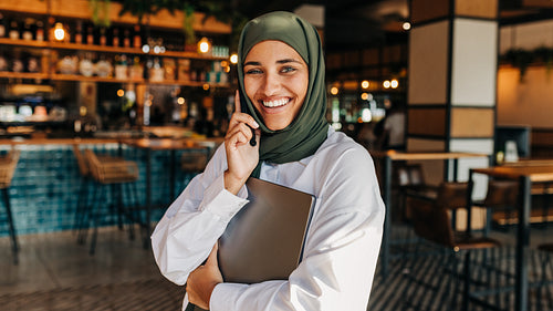 Happy Muslim freelancer making a phone call in a cafe
