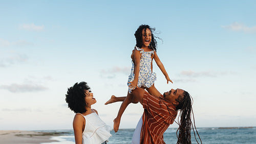 Happy family enjoying a beach vacation with parents lifting child in the air