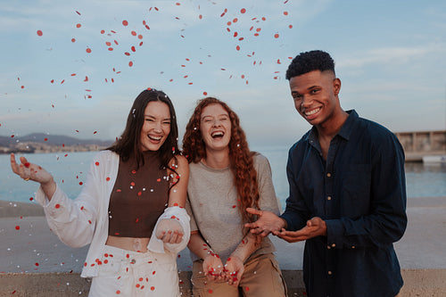 Cheerful friends celebrating red and white confetti outdoors
