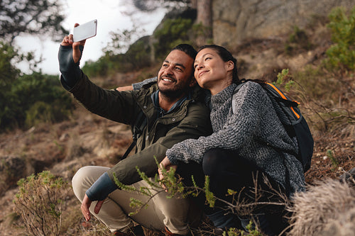 Couple sitting on mountain trail and taking selfie