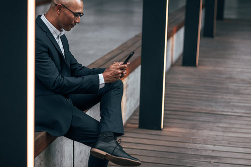 Businessman using mobile phone sitting outdoors