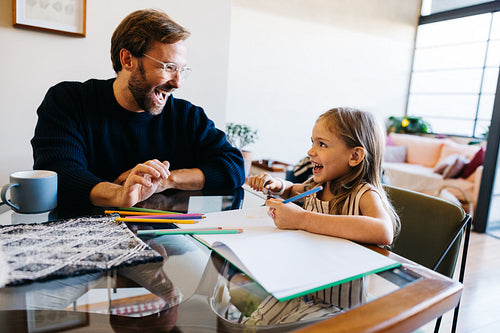 Father and daughter laughing while drawing with pencils at home