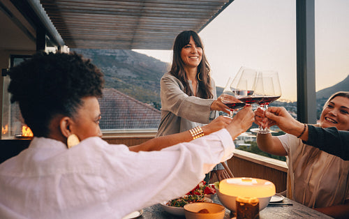 Group of friends toasting wine glasses on a terrace during sunset