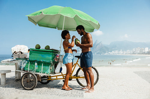 Couple enjoying coconut drinks by a vibrant beachside stand