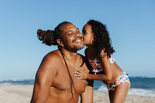 Loving moment between dad and daughter on the beach with a kiss