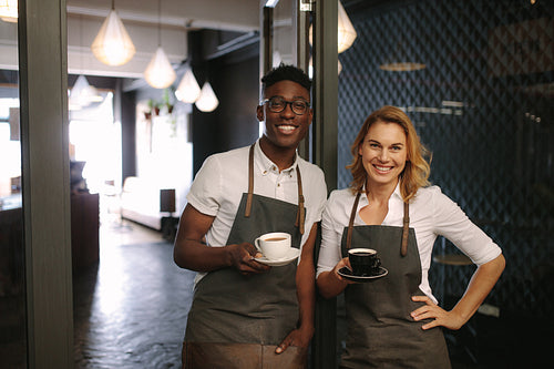 Café owners at their coffee shop holding coffee cups
