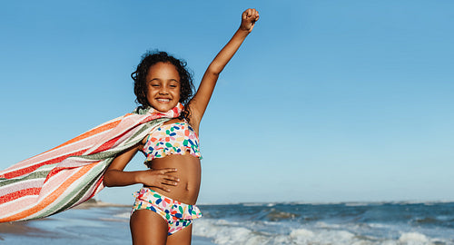 Proud young girl having fun at the beach with a towel cape on a sunny day