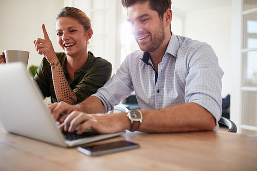 Cheerful young couple using laptop at home