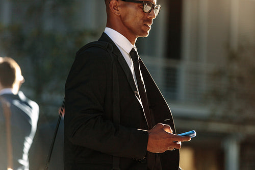 Man using mobile phone while walking on street to office