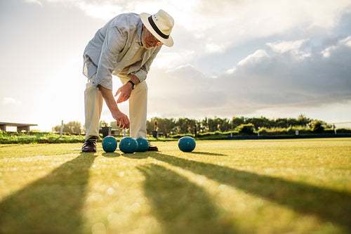 Old man picking a boules standing in a lawn