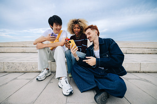 Three friends using their smartphones together outdoors on steps