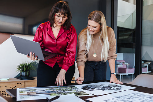Two women collaborating on architectural designs at a modern workplace using a laptop