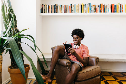 Happy teenage boy relaxing on a sofa, browsing social media on a tablet