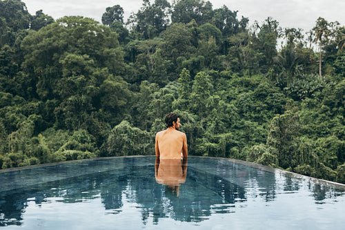 Young man standing in a infinity pool at resort