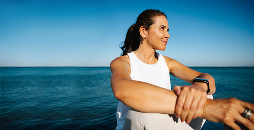 Confident woman stretching outdoors by the ocean under a bright blue sky