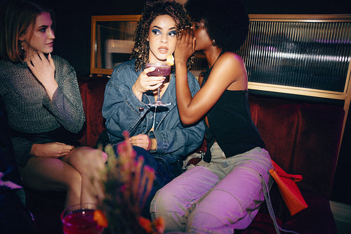 Three friends discussing secrets in a cozy bar booth setting