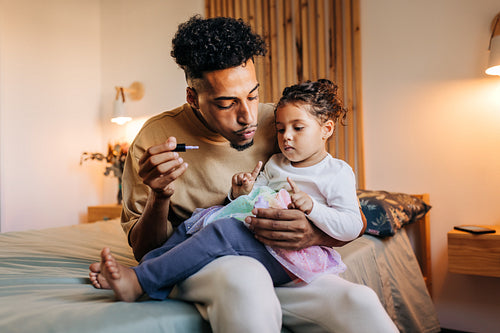 Single father blowing nail polish dry on his daughter's nails