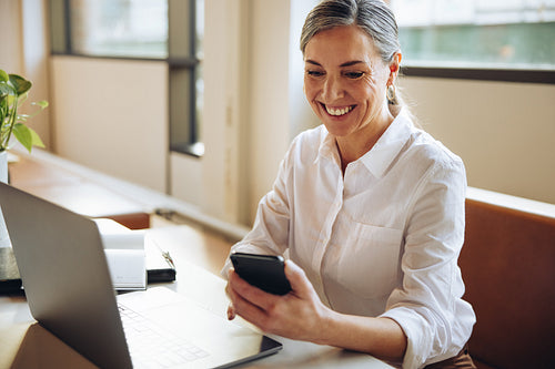 Cheerful businesswoman using cell phone in office