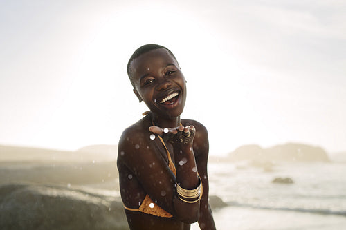 African girl blowing confetti from her hand on the beach