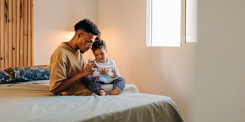 Father applying nail polish on his daughter's nails at home