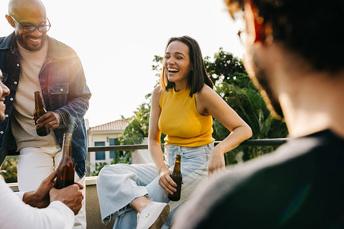 Friends enjoying laughter and beers on a sunny rooftop weekend
