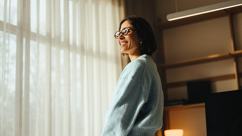 Standing woman looks away by a window in a home office