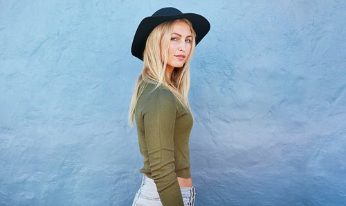 Stylish young female standing in front of a blue wall