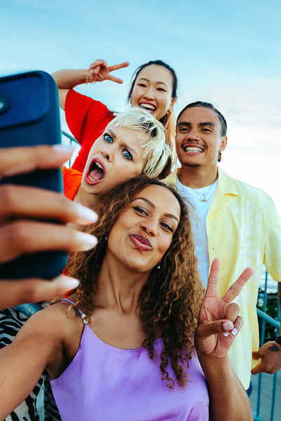 Posing friends hold a smartphone for a selfie outdoors beneath clear blue sky