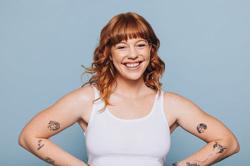 Portrait of a happy young woman with tattoos standing in a studio