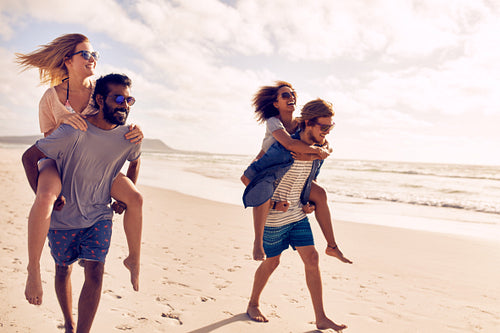 Couples piggybacking on sea shore