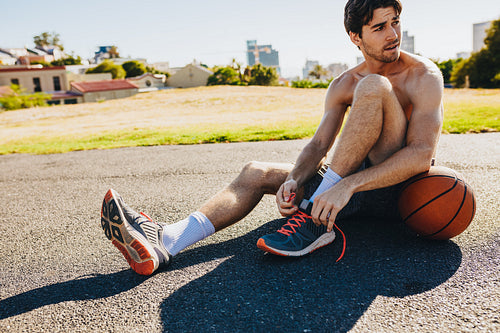 Basketball player tying shoe laces sitting on ground