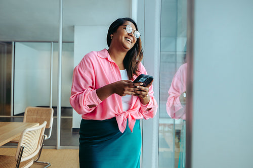 Confident Indian businesswoman in a modern office laughing while checking her smartphone