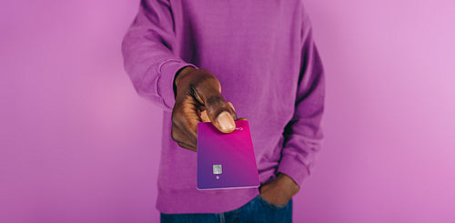 Tapping to pay, young man holds out a purple credit card to make a payment at checkout