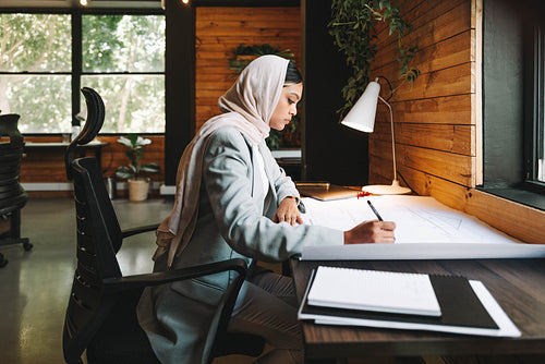 Muslim designer working on architectural blueprints in an office