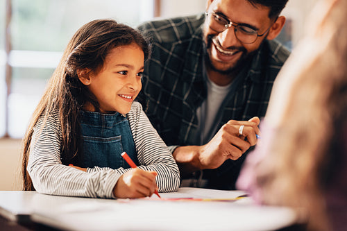 Mentoring children at elementary level. Girl smiles happily as she draws with the help of her teacher