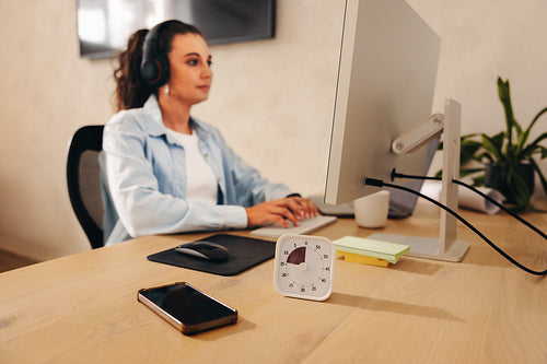 Focused businesswoman working at desk with timer and desktop computer