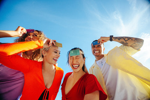Students hold payment cards on their foreheads while laughing together outdoors