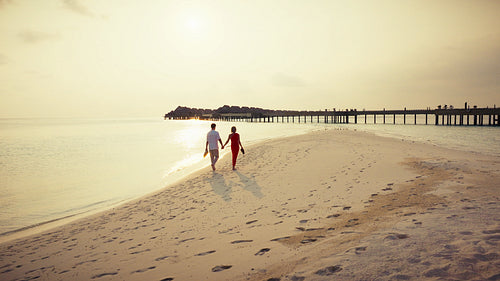 Romantic couple walking barefoot on a pristine beach at a luxury resort during golden hour