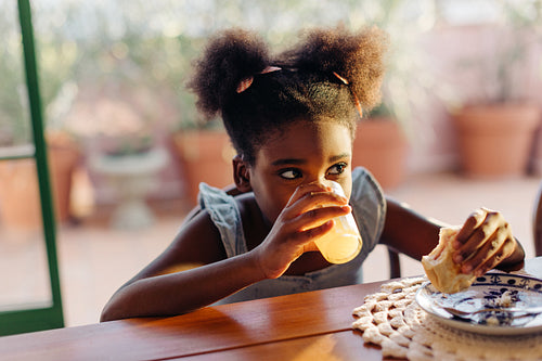 Afro-brazilian girl enjoying a delicious breakfast, drinking juice and eating pão de queijo