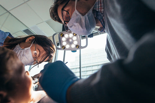 Dentist with assistant doing dental treatment on boy patient