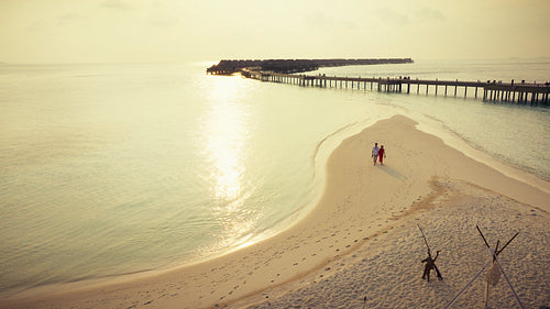 Romantic couple walking along beach toward sunset dinner setup