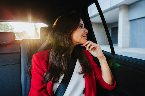 Businesswoman looking thoughtfully outside the car window at sunset