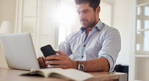 Man sitting at desk with laptop and mobile phone at home